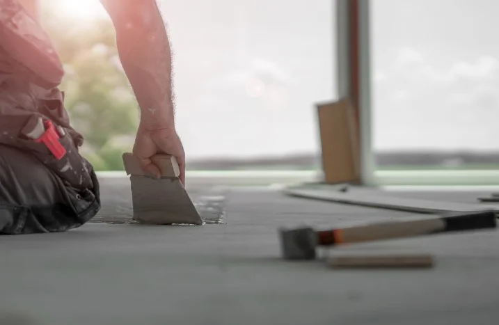 Person trägt Kleber mit Spachtel auf